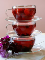 3 balanced cups and saucers of fruit tea with berries and flowers