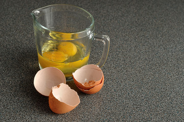 Two raw eggs in a measuring cup with egg shells