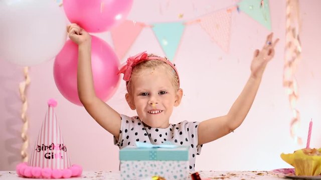 Happy birthday girl with colorful balloons and falling confetti having fun at party. Concept of celebration and excitement.
