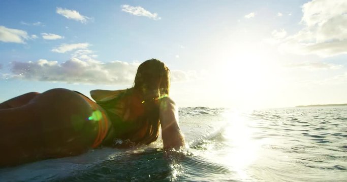 Beautiful surfer girl paddling into the sunset in slow motion