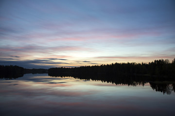 Calm evening at the lake. Some clouds are in the sky. Colorful sky. Silhouette forest.