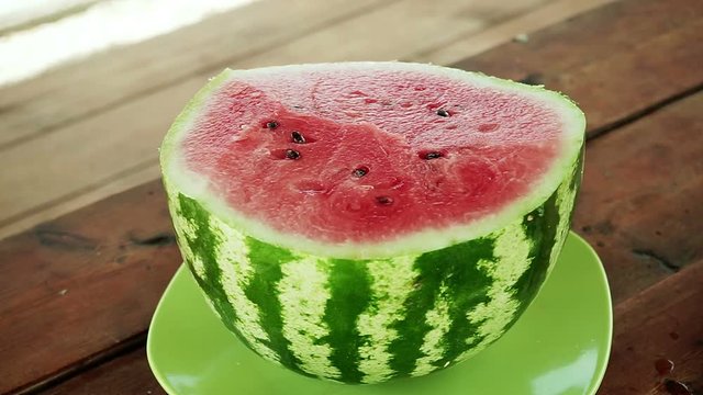Close-up shot of cut ripe juicy watermelon on the green plate standing on a wooden table. HD