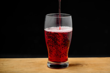 Cherry juice pouring into glass on wooden desk.