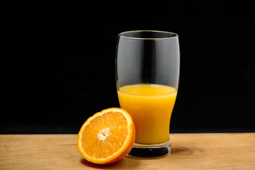 Glass of juice and half  orange on wooden desk.
