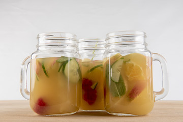 Three glass jars filled with fruit juice and pieces of cut up fruit. 
