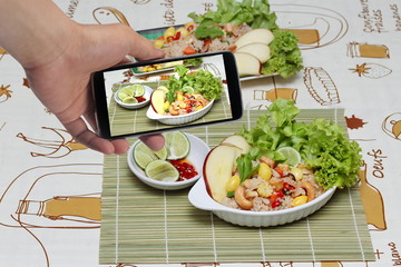 Using mobile phone to take photo a dish of Fried rice with mixed vegetable for share to social network. Selective focus.