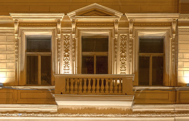 Fototapeta premium Three windows in a row and balcony on night illuminated facade of urban office building front view, St. Petersburg, Russia.