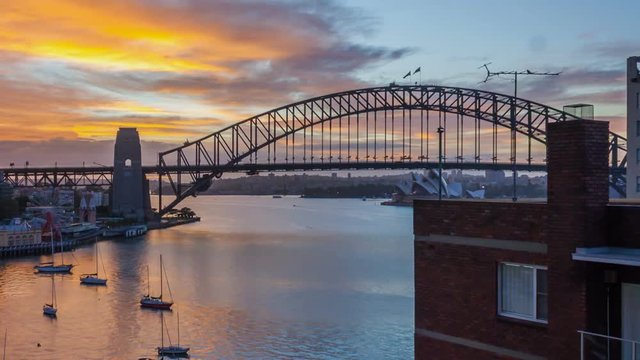 A beautiful sun rises over Sydney Harbour revealing the Bridge and Opera House. Time lapse. Tilt up