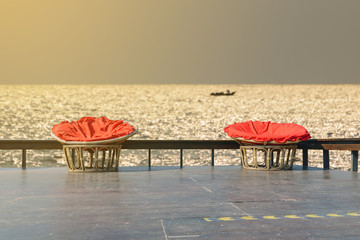 Chairs made of rattan and upholstery fabrics in red on wooden terrace with the backdrop of the ocean.