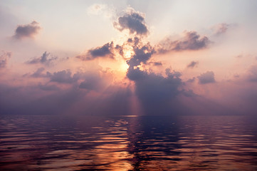 Sun shining through the clouds on sunrise in the sea.
