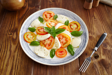 Caprese salad in a blue pastel plate on an old wooden table, with salt and pepper