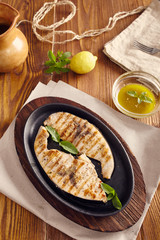 grilled swordfish slices in a cast iron pan on a wooden table, garnished with mint, oregano, salt and salmoriglio