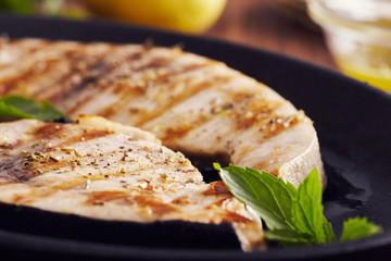 grilled swordfish slices in a cast iron pan on a wooden table, garnished with mint, oregano, salt...