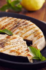grilled swordfish slices in a cast iron pan on a wooden table, garnished with mint, oregano, salt and salmoriglio