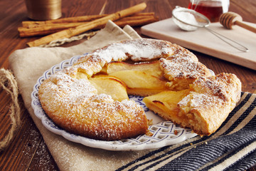 handmade apple pie on a dish over a napkin in a country style, cinnamon and hony in the background
