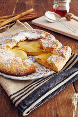 handmade apple pie on a dish over a napkin in a country style, cinnamon and hony in the background