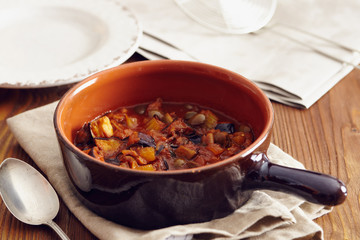 eggplant caponata, traditional sicilian dish. Served in a classic ceramic pan over a napkin on an aged wooden table. Surrounded by a silver spoon and a dish
