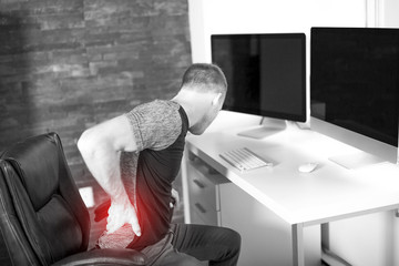 Man suffering from backache while sitting at computer desk in office