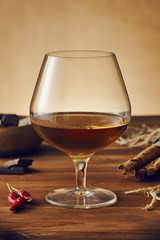 Glass of brandy on a old wooden table with a bowl with chocolate, cinnamon stiks and chili peppers. Warm background.