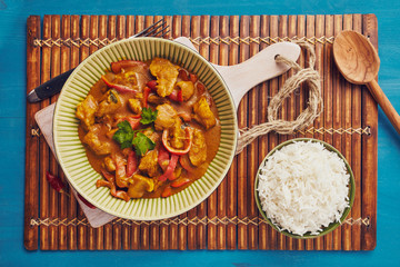 Curry chopped pork in a bowl with basmati rice on a bamboo placemat on a blue wooden table