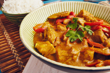 Curry chopped pork in a bowl with basmati rice on a bamboo placemat on a blue wooden table