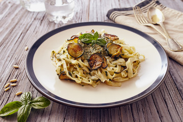 handmade fettuccine pasta with pesto genovese sauce and fried courgette on white dish with a blue border, on a wooden table
