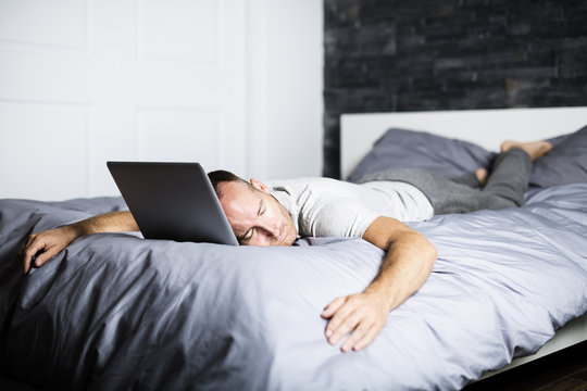 Man Sleeping Over Laptop Computer In Bed