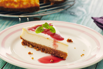 new york cheesecake with cherry sauce on a plate on a blue wooden table, full cake in background