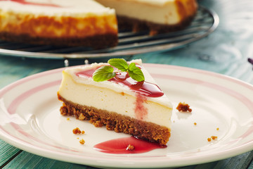 new york cheesecake with cherry sauce on a plate on a blue wooden table, full cake in background