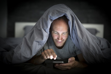 young cell phone addict man awake late at night in bed using smartphone
