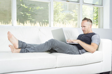 Front view of a handsome man using  laptop sitting on couch at home