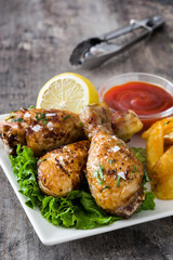 Roast chicken drumsticks and chips on wooden table

