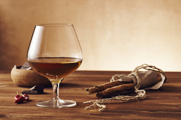 Glass of brandy on a old wooden table with a bowl with chocolate, cinnamon stiks and chili peppers. Warm background.