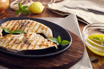 grilled swordfish slices in a cast iron pan on a wooden table, garnished with mint, oregano, salt and salmoriglio - obrazy, fototapety, plakaty