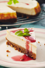 new york cheesecake with cherry sauce on a plate on a blue wooden table, full cake in background