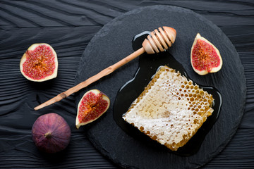 Honeycomb, liquid honey and figs on a black wooden background
