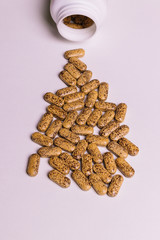 Brown pills and upside down bottle on a pink background