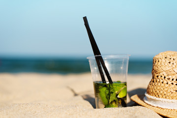 Mojito cocktail on the beach and straw hat. Blurred beach background with copy space. Sun, sun haze, glare