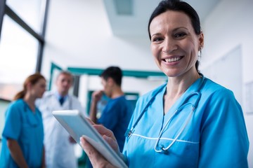 Portrait of smiling surgeon using digital tablet in corridor