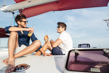 Two men friends drinking beer while resting on the yacht