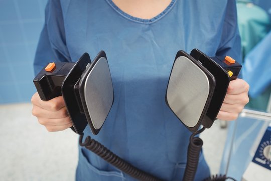 Mid section of female surgeon holding defibrillator