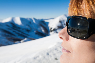 visage de femme avec des lunettes de soleil dans la neige face aux montagnes