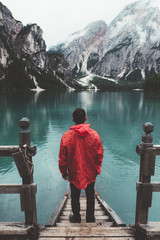 man with red raincoat on wood pier at lake braies with mountains on the background - 121567281