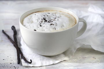 Latte coffee. Vanilla. Light colored old wooden background. Vanilla bean and white fabric. Light illumination.