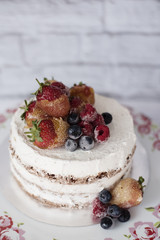 Naked cake with caramelized fruits - strawberries, blueberries, raspberries. Sponge cream cake in floral high plateau, tray. Rustic background