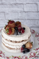 Naked cake with caramelized fruits - strawberries, blueberries, raspberries. Sponge cream cake in floral high plateau, tray. Rustic background