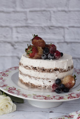 Naked cake with caramelized fruits - strawberries, blueberries, raspberries. Sponge cream cake in floral high plateau, tray. White roses, rustic background