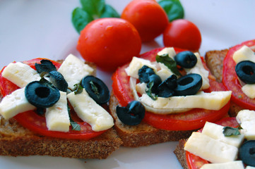 Bruschetta with tomatoes, black olives, goat cheese, herbs and oil on toasted bread