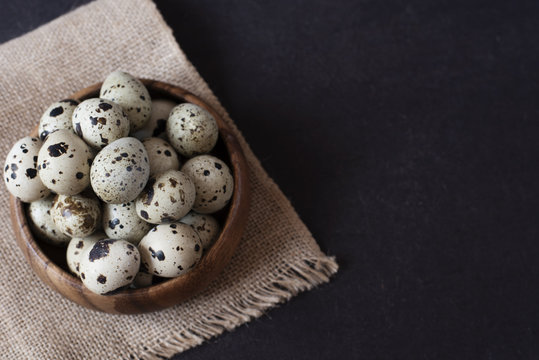 Wooden bowl with quail eggs. Dark food photography. Rustic background, selective focus and diffused natural light. A different type of concept image for Easter. Copy space.