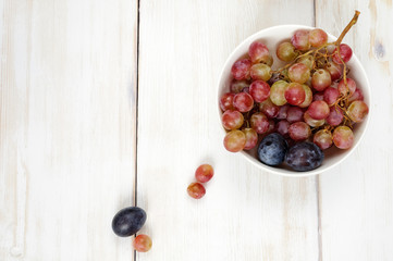 Plums and grapes in bowl on the white wooden table